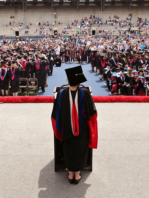 Woman in cap and gown standing on stage facing crowd of students in caps and gowns