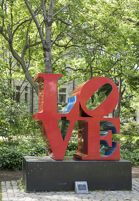 The iconic red LOVE sculpture appears amidst green foliage on Penn’s campus.