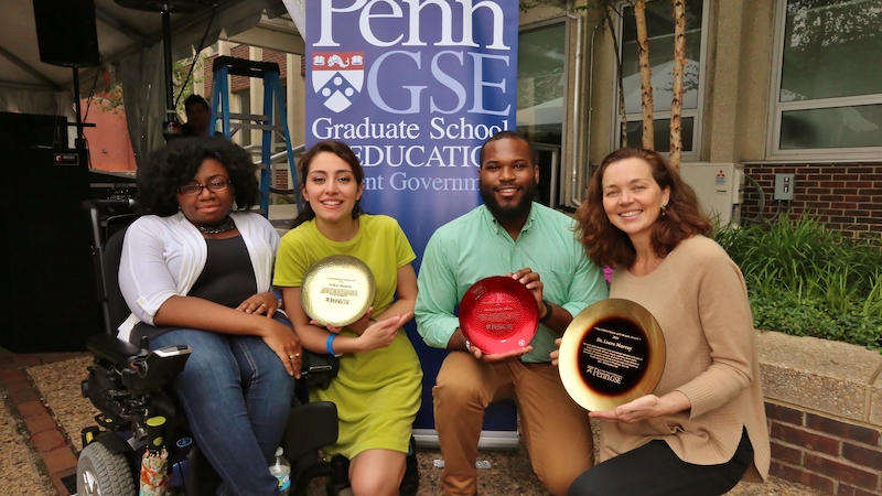 A representative from GSE Student Government poses with 3 student award recipients, who are holding their award plates