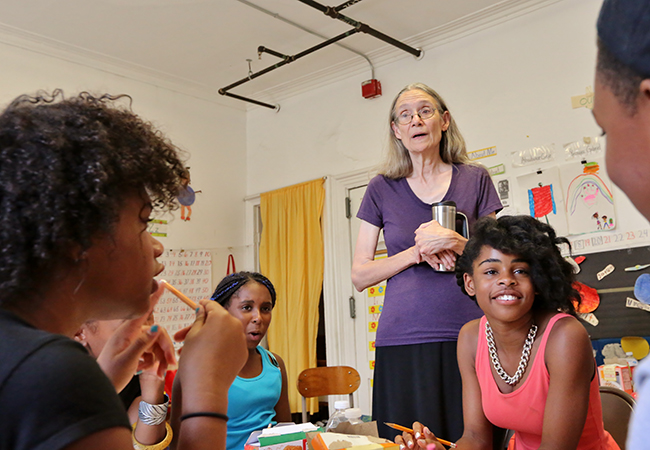 Woman with long hair and glasses, young boy sitting and speaking, young girl looking.