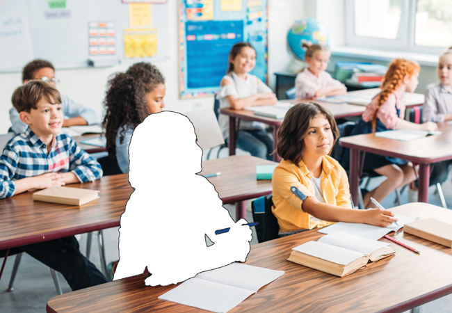 Children sit at long tables in an elementary school classroom, but one of them is missing.