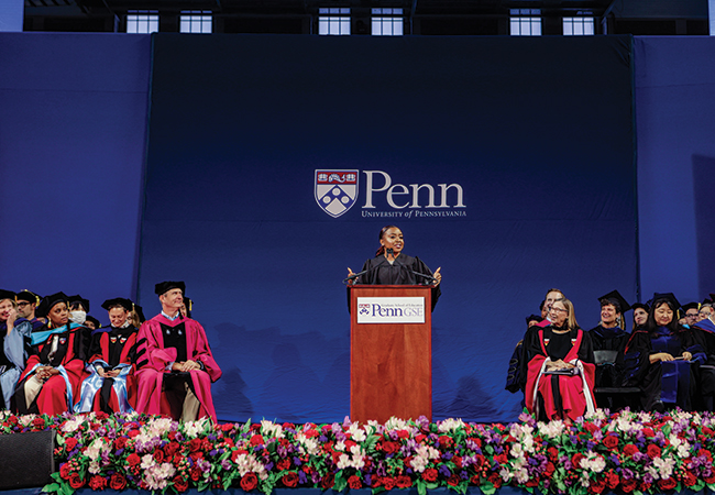 Abbott Elementary creator Quinta Brunson stands at a podium flanked on either side by Penn GSE faculty while delivering remarks at the 2023 commencement ceremony.