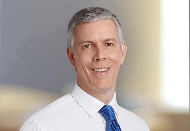 A headshot of Arne Duncan in a white button-down shirt and blue tie