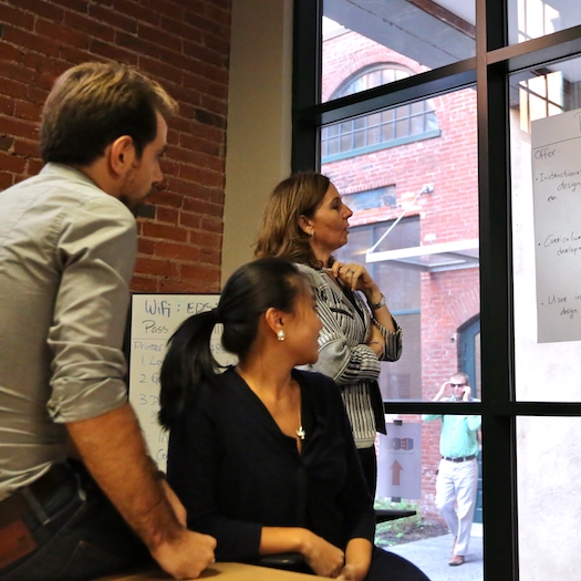 Two women and one man looking intently at chart taped to a window.