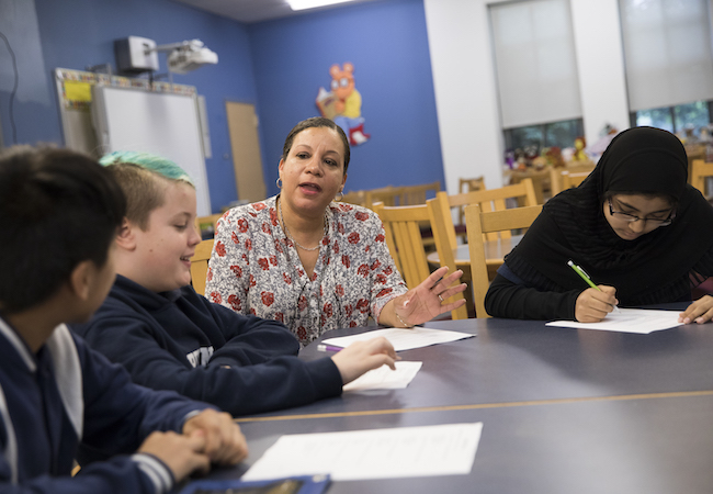 A teacher and students sit around a table, before COVID-19.