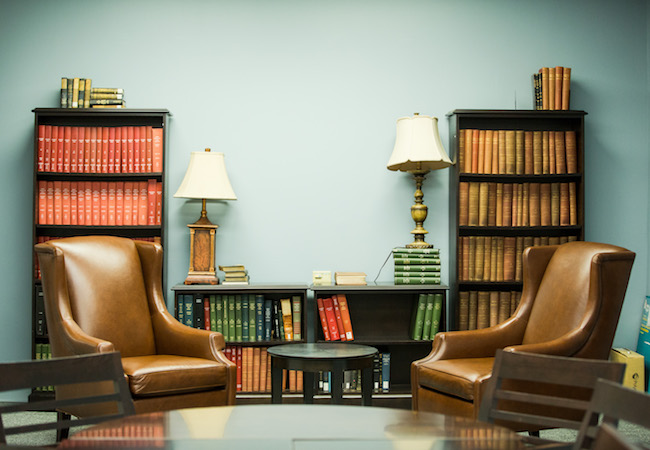 A boardroom with two empty large leather chairs in front of bookcases.