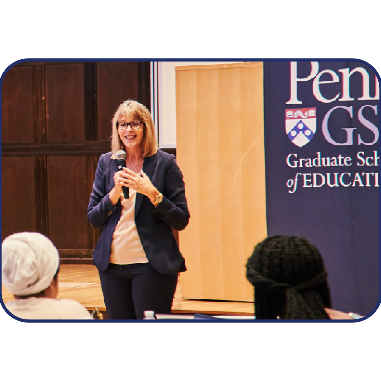 Catherine Jerie holds a microphone andspeaks in front of a Penn GSE banner to aneducational entrepreneurship class.