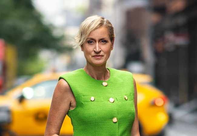 Kandi stands in a New York City street in a bright green top in front of a yellow taxi.