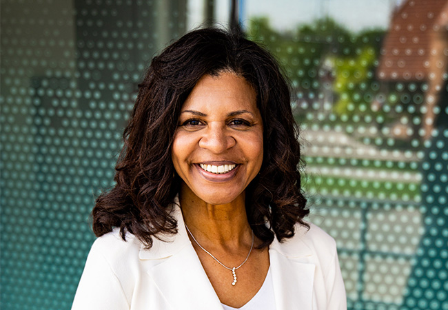 Dr. Cheryl Logan in a white suit smiles warmly, standing before a glass front building