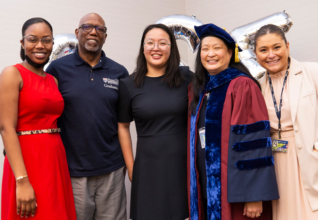 Members of the Office of Student Success stand with a professor in full academic regalia in front of GSE balloons.