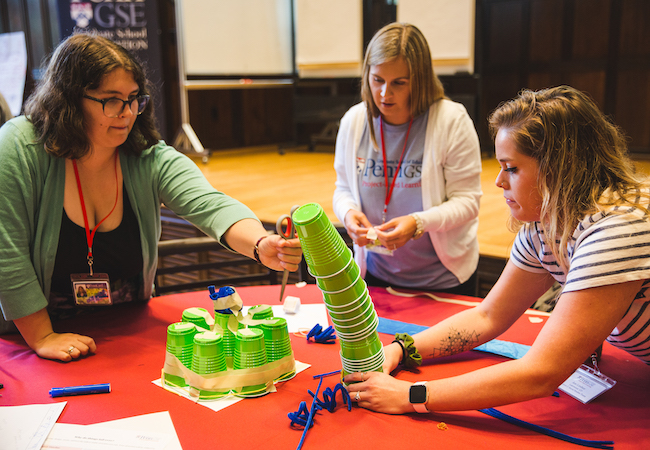 A group of educators attempts to stack cups on a table during a project-based learning professional development workshop. 