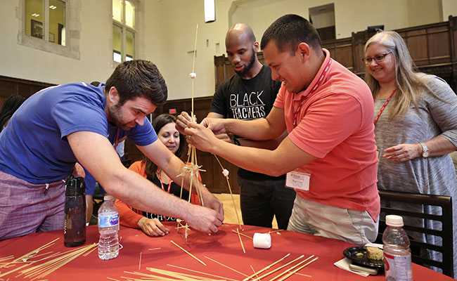 Several people working together to build a structure on top of a table