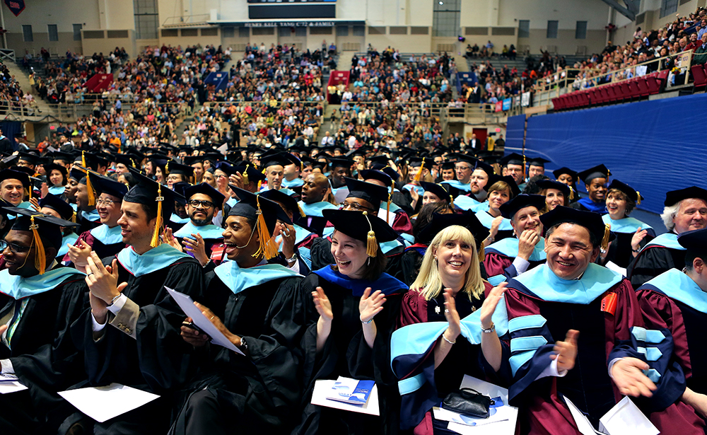 Students in caps and gowns sitting and clapping