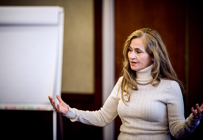 Woman in tan sweater standing and speaking.