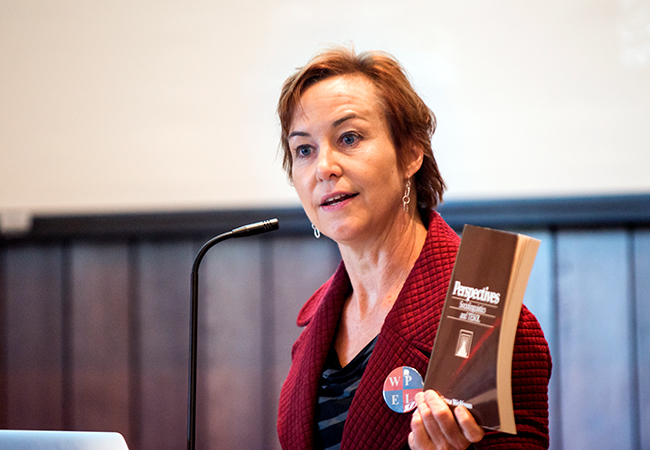 Woman speaking at microphone with book in hand.