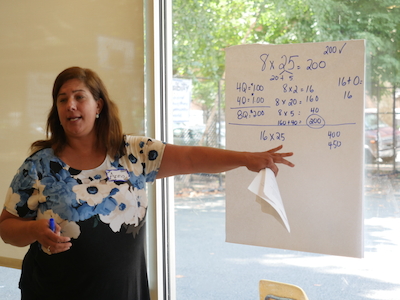 A teacher in the Responsive Math Teaching program points to a poster where she has written out solutions to a multiplication math problem.