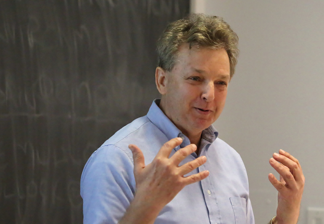 Richard Ingersoll gestures with both hands, standing in front of a chalkboard.