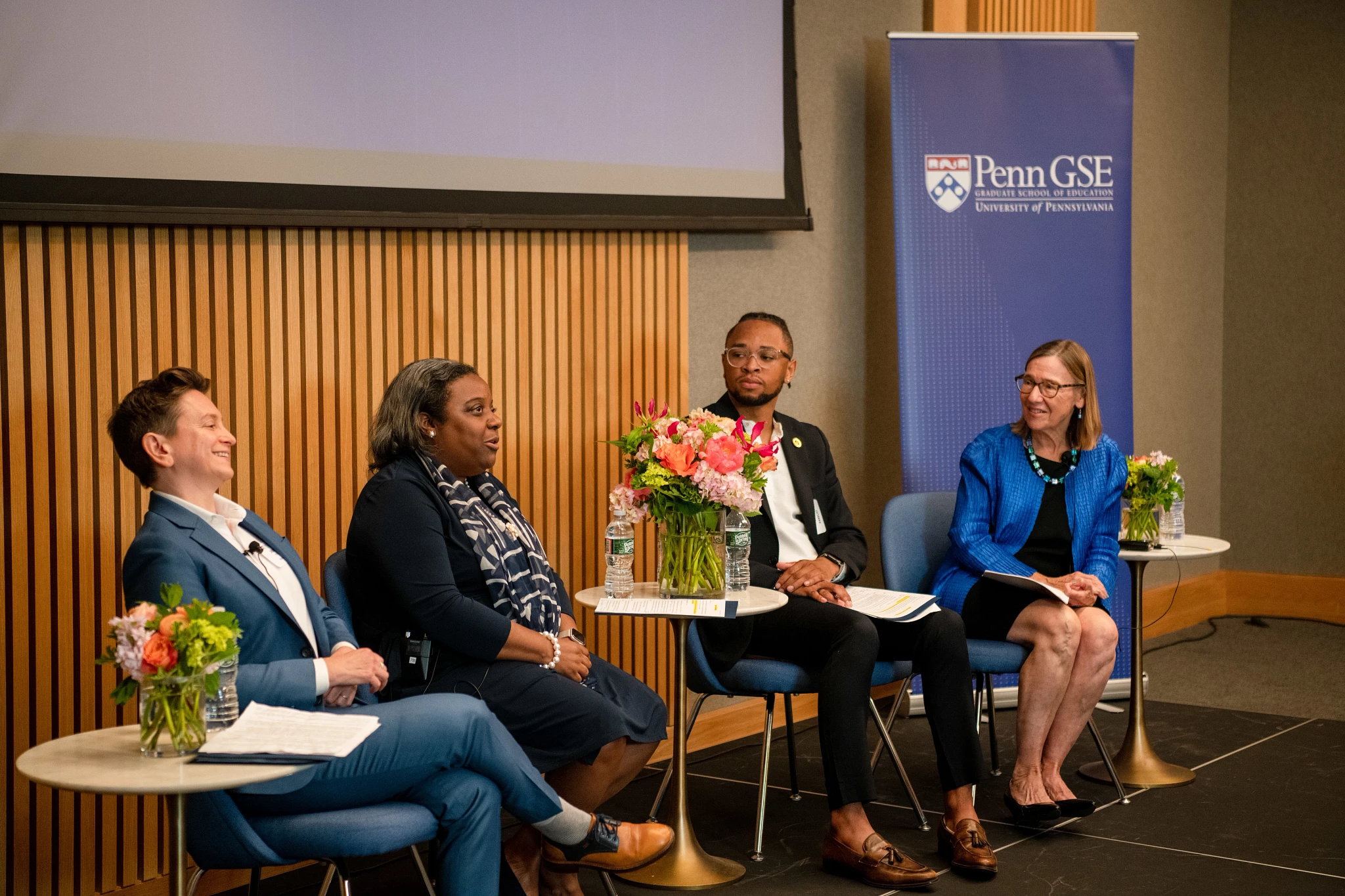 The four panelists look at each other and smile while engaged in conversation, sitting in front of a Penn GSE banner.