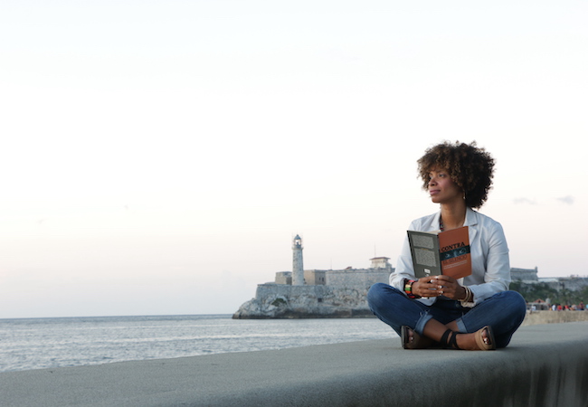 Amalia Dache sits on a ledge overlooking a harbor during a research trip to Cuba. 