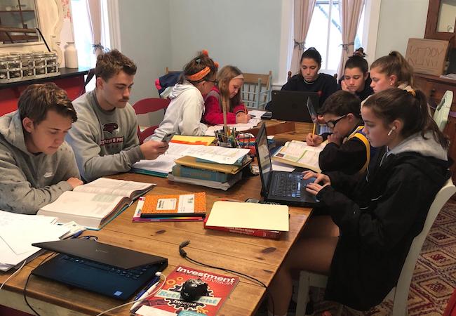 A family crowds around a dining room table working on homework.