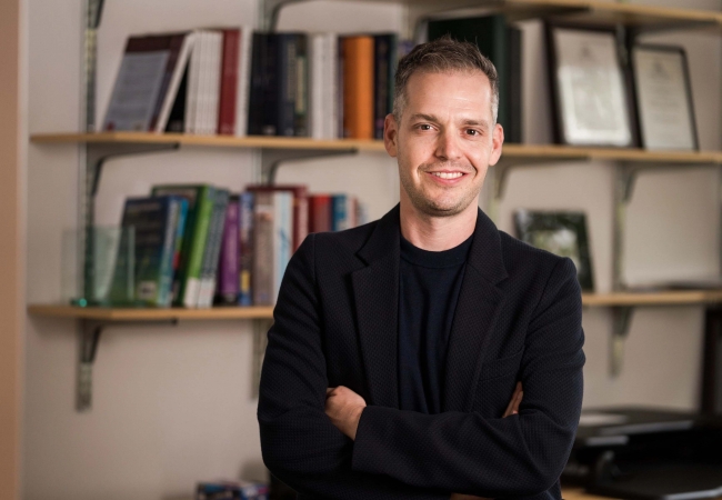 Man with crossed arms in front of bookshelf