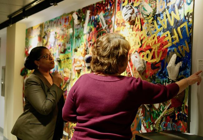 Two women look at the painting Education Not Incarceration. 