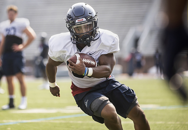 A Penn football player running with a football.