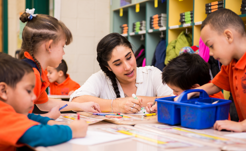 A kindergarten teacher with students using crayons at a table