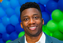 Headshot of a smiling man in a blazer in front of a background of balloons