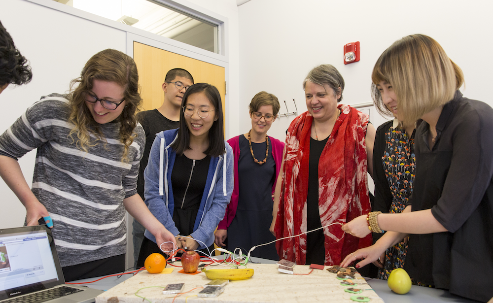 Professor and students smiling as they connect electronic sensors to fruits and other objects