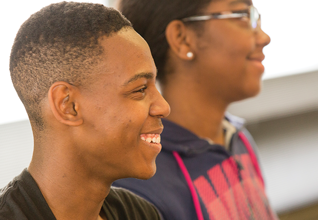 Two high school students in a classroom look ahead and smile.