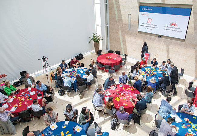 Above view of several round tables with groups sitting and engaging in an activity with sticky notes