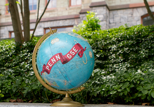 A globe with a banner that says Penn GSE is sitting outdoors next to green hedges