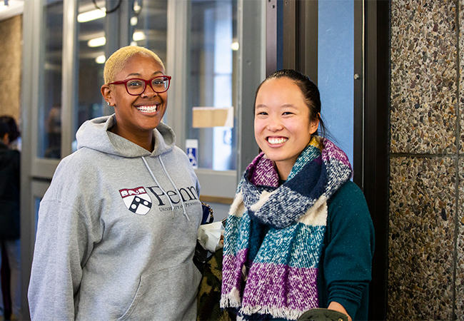 Two people at an alumni event looking at the camera, one in a Penn sweatshirt and the other with a colorful scarf