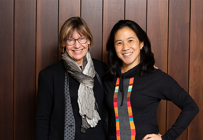 Dean Pam Grossman and Angela Duckworth stand in front of a wood paneled wall smiling at the camera