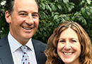 A man in a suit and tie and a woman in a black blouse smiling while standing outdoors