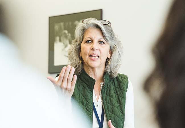 Faculty member Caroline Watts is seen between two listeners, speaking in a classroom.