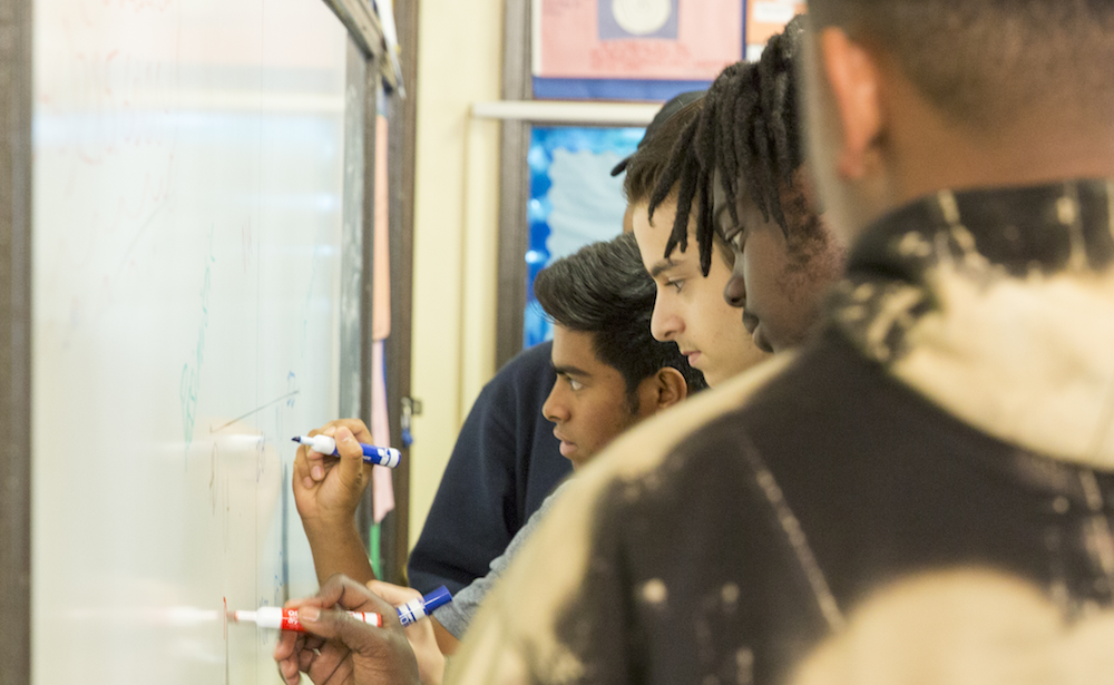 Philadelphia high school students shown in profile writing on a whiteboard