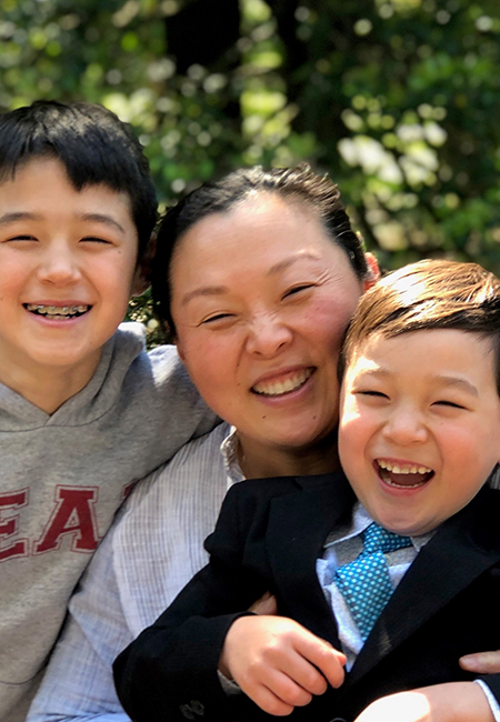 Melissa Kim smiles in between two smiling children outdoors