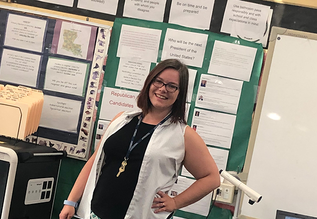 Sarah Cannon-Straight stands in a classroom in front of a bulletin board