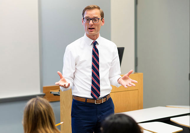 A man in professional attire speaks to students in a classroom