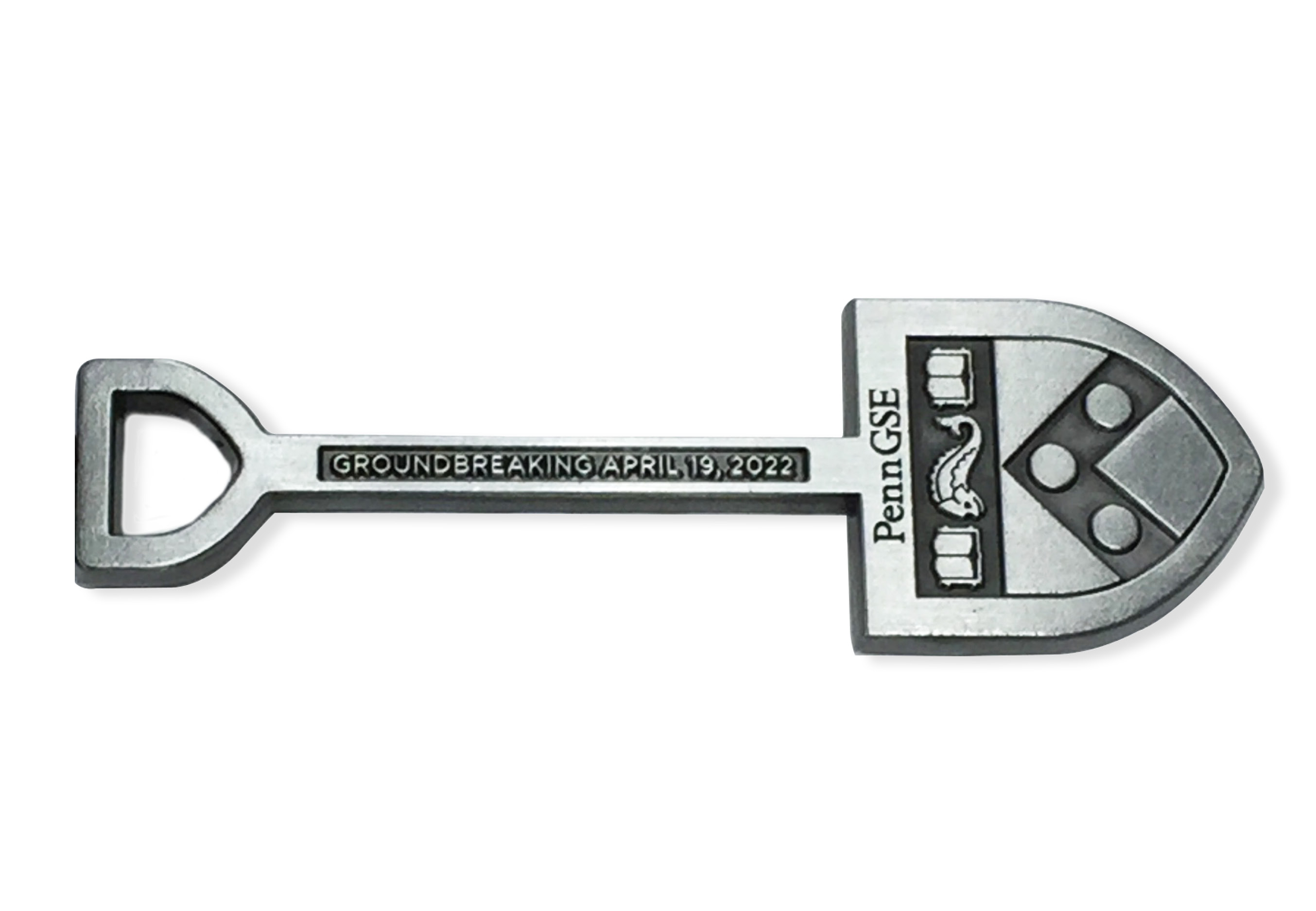 A silver keychain fob in the shape of a shovel has the Penn shield and “Penn GSE” on the spade and “Groundbreaking April 19, 2022” on the handle.