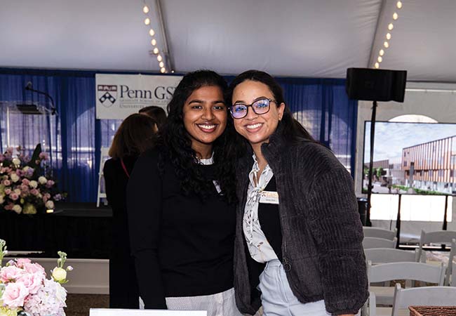 Two individuals, smiling, stand together behind a registration desk. The Penn GSE logo is seen in the background.