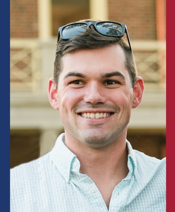 A man in front of a brick background smiles and looks into the distance. Blue and red bars appear on the right and left of the photo.