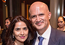 A woman in a pink blouse and a man in a suit and tie smiling while standing indoors