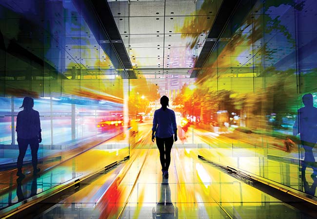 Silhouette of a woman walking through a tunnel of glass that reflects different colors of scattered light.