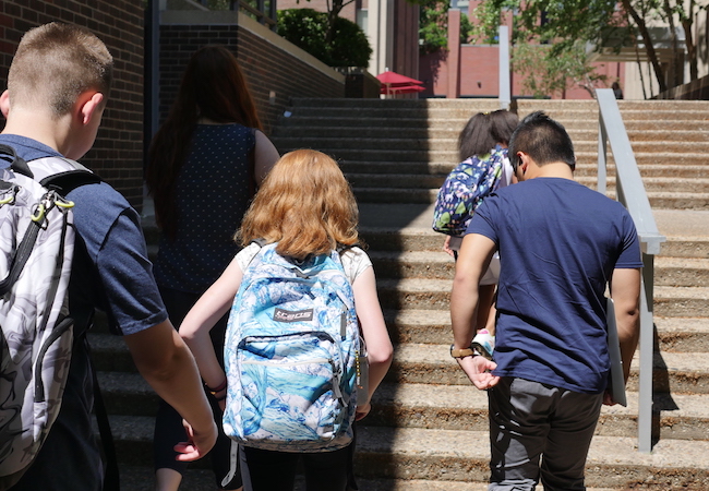 Students with backpacks walking up school steps