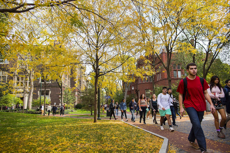 Penn students walk along a campus pathway among the autumn colors.