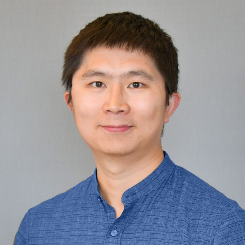 An asian man looks into the camera with a slight smile and a button up blue shirt