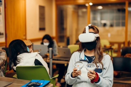 Student wearing VR headset and holding control paddles inside the VR studio.